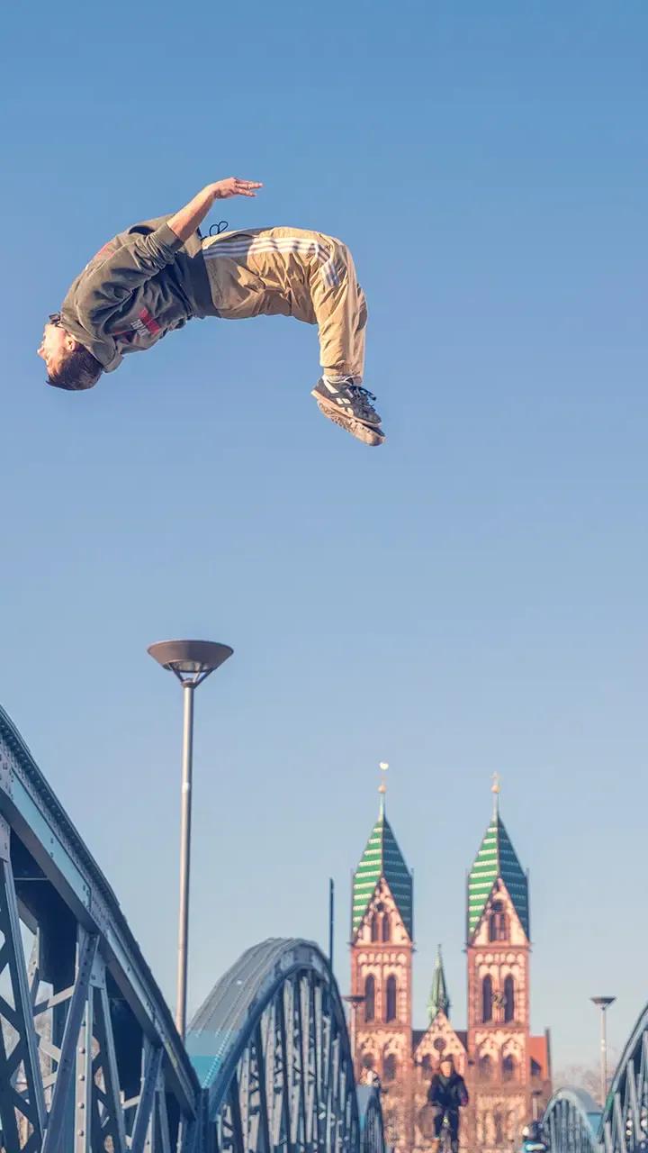 Parkour-Salto über der Wiwilíbrücke in Freiburg, dahinter die Herz-Jesu-Kirche